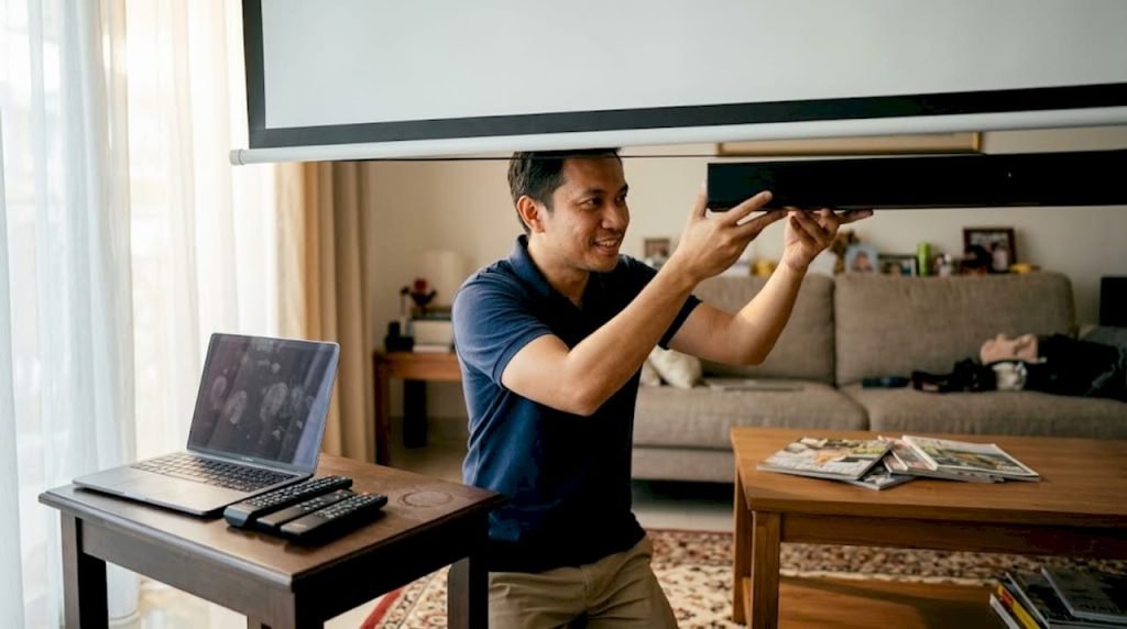 Man adjusting soundbar under home projector screen